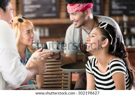 Waiter serving coffee in Asian cafe to women and man offering the drinks on a tray