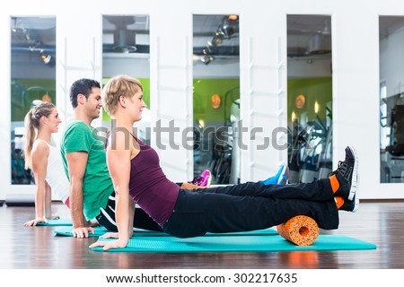 Group of one man and two women doing roll gymnastics on floor of gym or fitness club