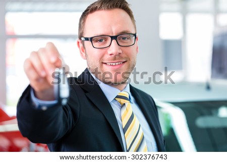 Salesman handing over auto key at car dealership