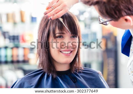 Hairdresser cutting woman hair in shop