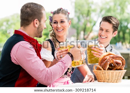 Friends in beer garden clinking glasses with beer, pretzel standing on the table