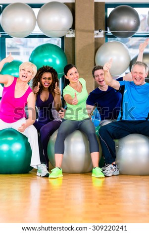 Men and women sitting on fitness balls in gym, diversity group of old, young, black and white people
