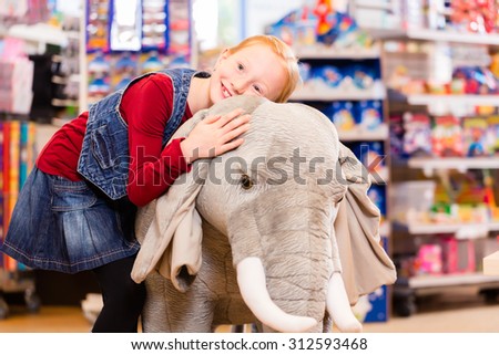Little girl in toy store cuddling with stuffed animal, shelves with toys in the background