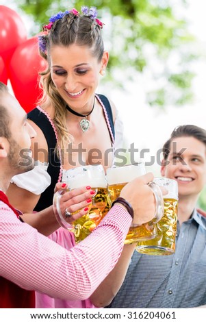 Three friends in Munich Beer garden clinking glasses wearing traditional Tracht