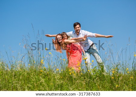 Family doing the plane on summer meadow under clear blue sky