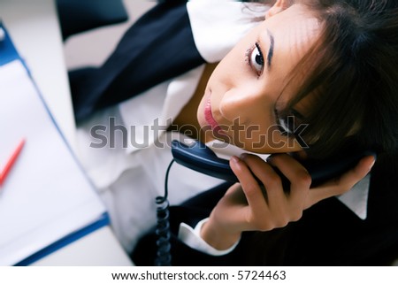 Latina in the office, phoning, looking at the viewer