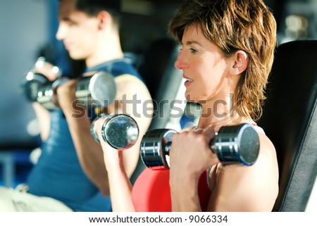 Couple (male / female) lifting dumbbells in a gym; focus on face of the woman