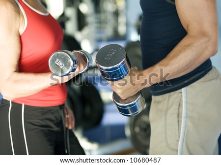 A man and a woman (only arms and body) lifting dumbbells (shallow depth of field, focus only on hands)
