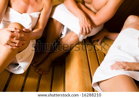 Three people, one male, two female, enjoying a hot sauna (no faces, focus on hand of man)