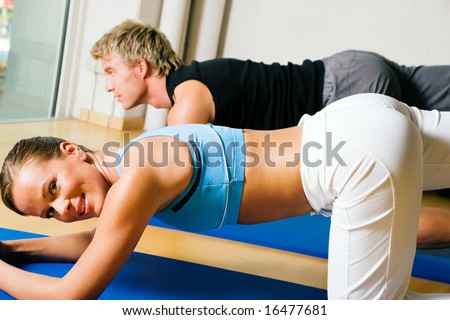 Couple in a gym performing gymnastics that are supposed to make a sexy ass. Judging from the models it might work.