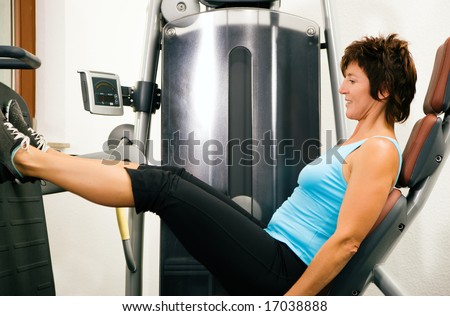 Young man in a gym training his back muscles on a machine Mature woman exercising her legs at a machine in the gym