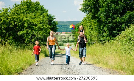 Family walking down a path on a bright summer day, a village in the background