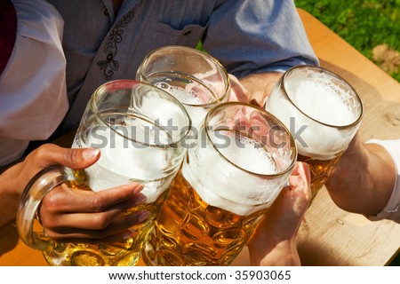 Group of four people in Couple in traditional Bavarian dress, Lederhosen and Dirndl, in a beer garden or at a festival like the Oktoberfest; focus on beer steins