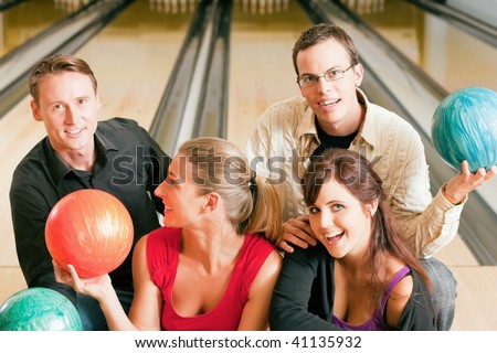 Group of four friends in a bowling alley having fun, holding their bowling balls and flirting with each other (focus on girls in front row)