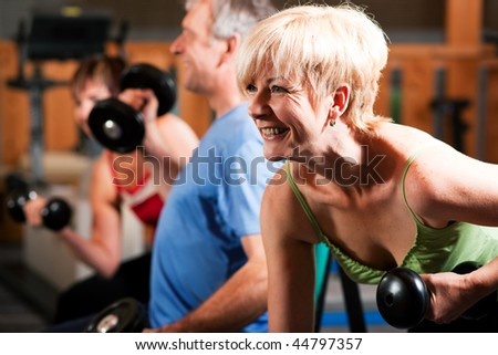 Three senior people - two women and one man - in the gym lifting dumbbells, exercising