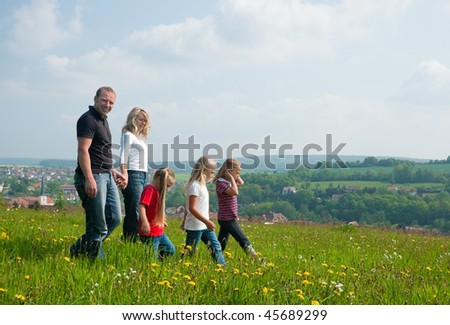 Happy family with Children walking down a meadow with dandelion flowers at a bright spring day, in the background a village is to be seen