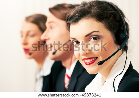 Group of three customer care representatives in a call center with headphones rendering service to callers