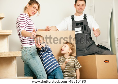 Family moving in their new house. They are standing in front of a stack of moving boxes being happy. Father is dressed in a way that can also represent a mover