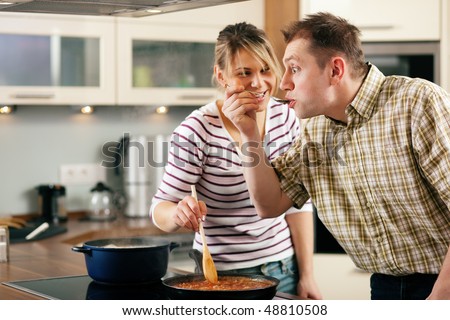 Couple cooking together in their kitchen, the man tasting the sauce finding it very hot and spicy - as you can tell by his facial expression