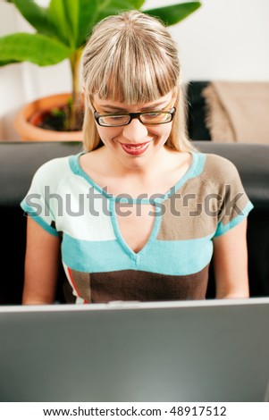Woman - a telecommuter - doing administration of her business from a laptop sitting on a sofa in her living room