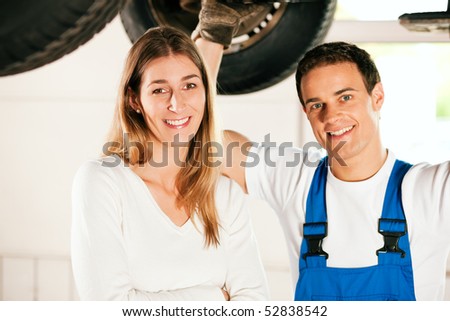 Woman standing in front of her car which is lifted on an auto hoist, a mechanic doing a repair underneath the auto