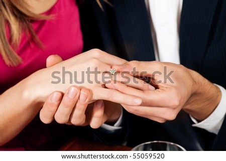 Man gently sticks a diamond ring on the finger of his fiance after a romantic dinner (just hands to be seen)