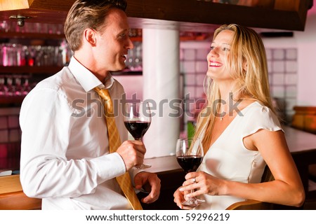Two (casual) business people in a hotel bar in the evening having glasses of red wine and a little flirt