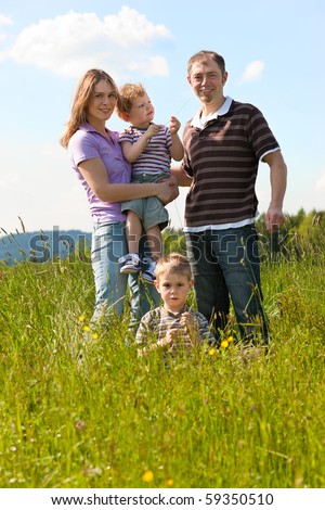 Family with two little boys playing in the grass on a summer meadow carrying one of the kids