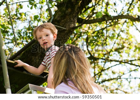 Little boy and his mother climbing up a ladder, they want to reach their tree house (house not to be seen)