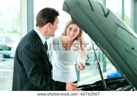 Woman buying a car in dealership looking under the hood at the engine