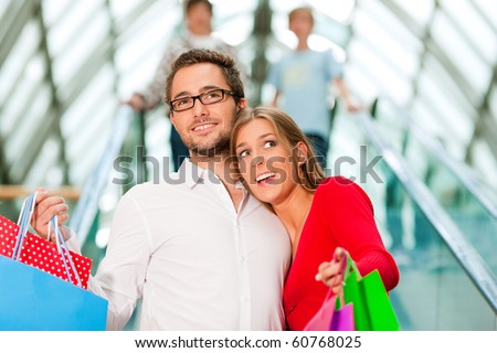 Couple - man and woman - in a shopping mall with colorful bags on an escalator