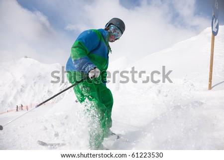 Man on a ski track going downhill, stopping in front of camera dusting some snow