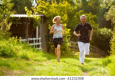 Mature or senior couple doing sport outdoors, jogging down a path in summer, the sun is low on evening