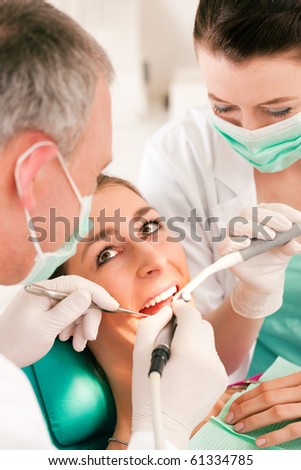 Female patient with dentist and assistant in a dental treatment, wearing masks and gloves, Dentist and assistant bowing over her using sucker and drill