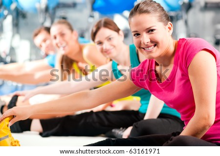 Group of four people in colorful cloths in a gym doing aerobics or warming up with gymnastics and stretching exercises