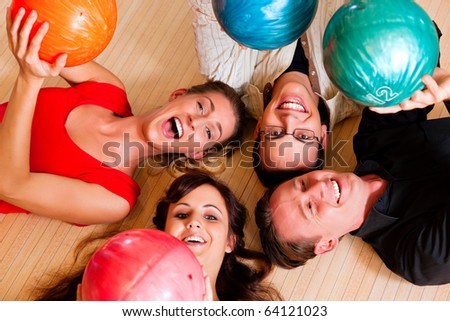 Group of four friends lying in a bowling alley having fun, holding their bowling balls above them