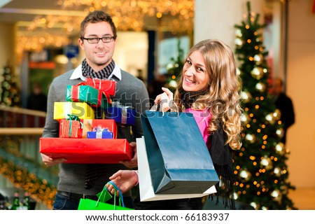 Couple - Caucasian man and woman - with Christmas presents, gifts and shopping bags - in a mall in front of a Christmas tree