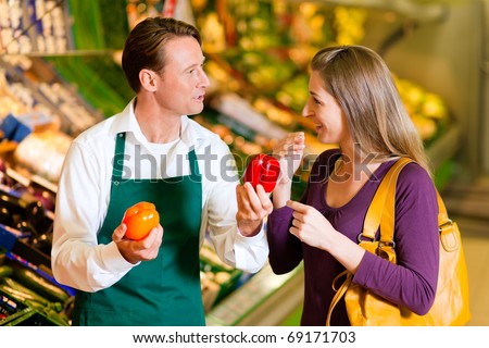 woman in a supermarket at the vegetable shelf shopping for groceries, a shop assistant is helping her