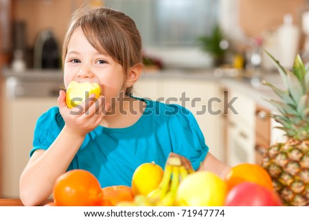 Healthy eating - child eating an apple, lots of fresh fruit on the table in front