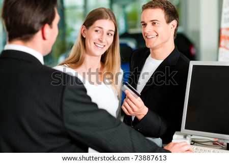 Sales situation in a car dealership, the young couple is giving the credit card to pay for the new car
