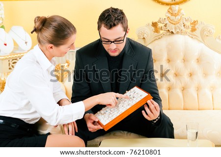 Man choosing a ring at the jeweller and gets consultancy by a shop assistant