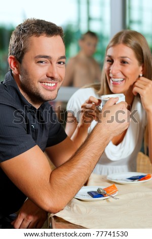 Young couple - man and woman - drinking coffee in a cafe in front of a glass facade