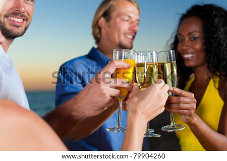 People (two couples) on the beach having a party, drinking and having a lot of fun in the sunset, they are wearing smart casual clothes and drink champagne