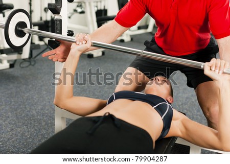 Woman in gym with personal fitness trainer exercising power gymnastics with a barbell