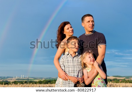 Happy family - mother, father, children - standing under a Rainbow in summer looking into a glorious future