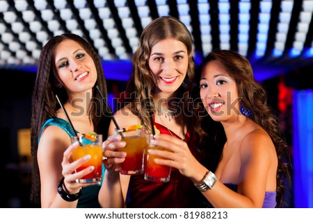Group of party people - three friends - with cocktails in a bar or club having fun
