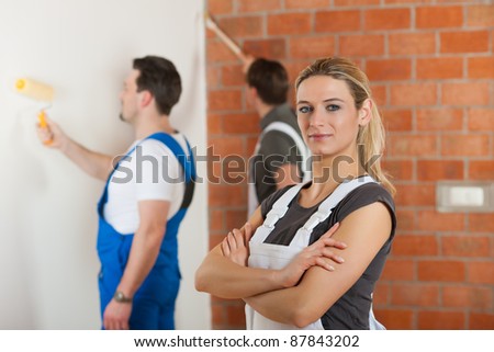 Three people - one woman and two men - renovating an apartment; the woman is standing with arms crossed in front
