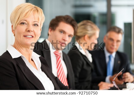 Business - team in an office; the female boss is looking into the camera