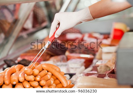 Working in a butcher\'s shop - a shop assistant is packing sausages (only hands to be seen)  fork for selling
