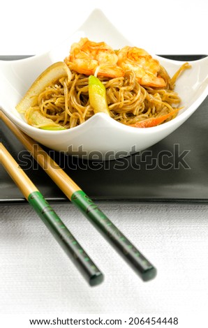 Delicious Chinese noodles topped with shrimps served in a stylish contemporary white porcelain bowl on a square black plate with chopsticks for healthy seafood cuisine, studio shot on white